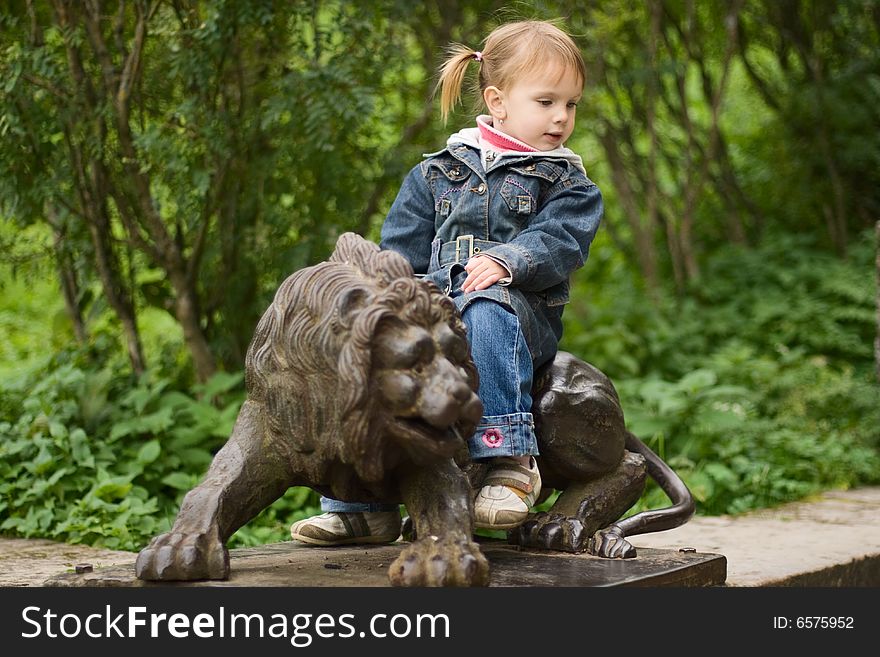 Small funny girl sitting on lion sculpture at the park. Small funny girl sitting on lion sculpture at the park