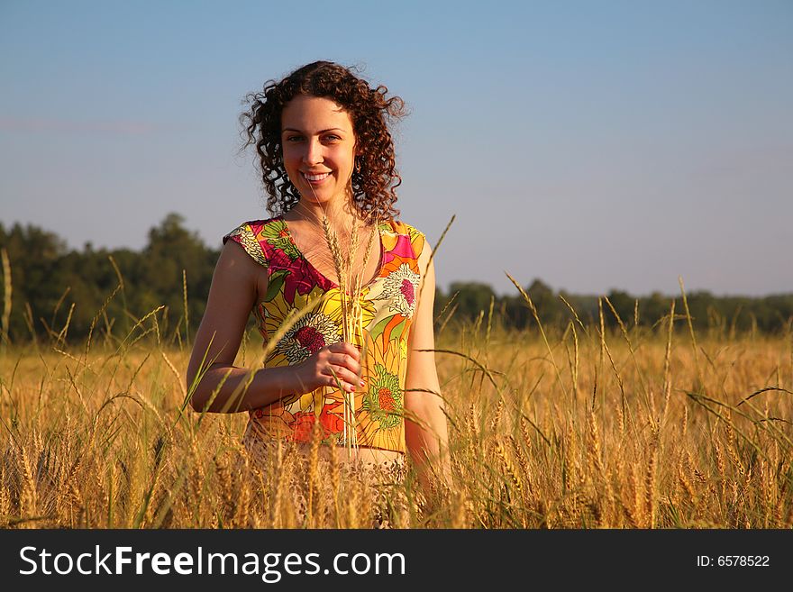 Young woman with earns stands on a wheaten field