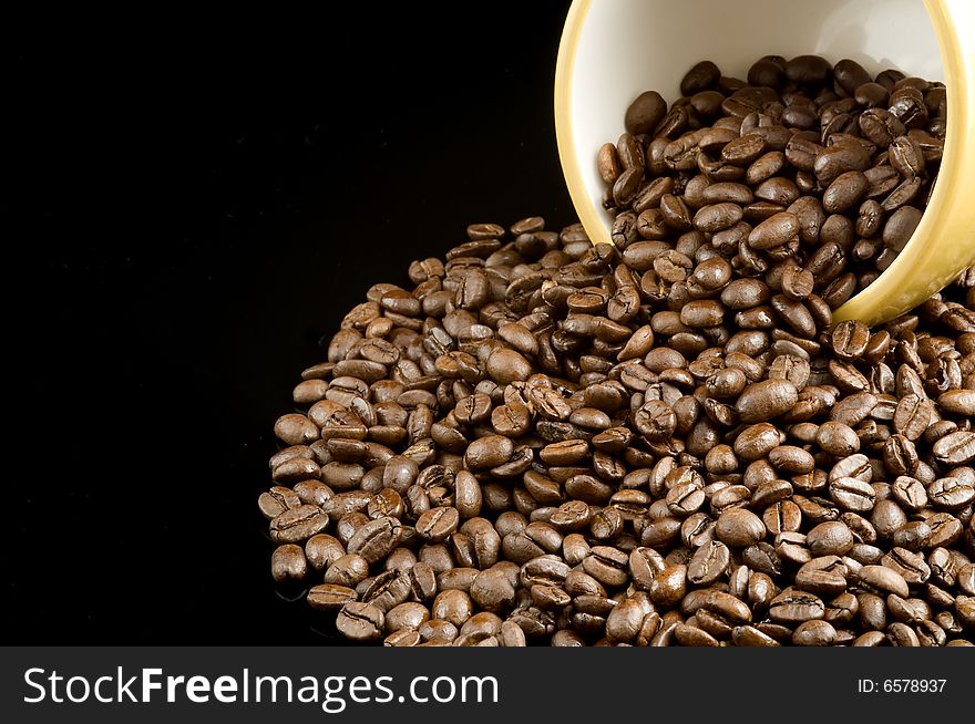 Spilled coffee beans from a yellow bowl on a black background