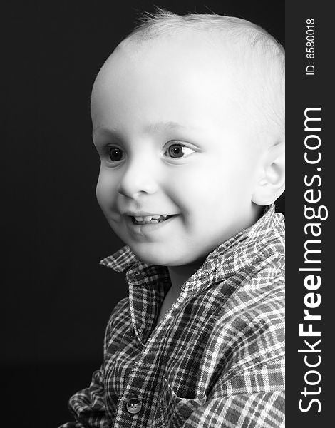 Blonde toddler against a black background with a big smile