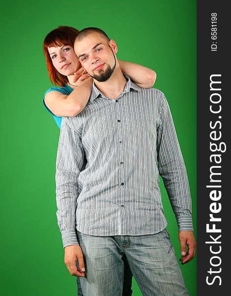 Girl with red hair embraces guy behind on green wall