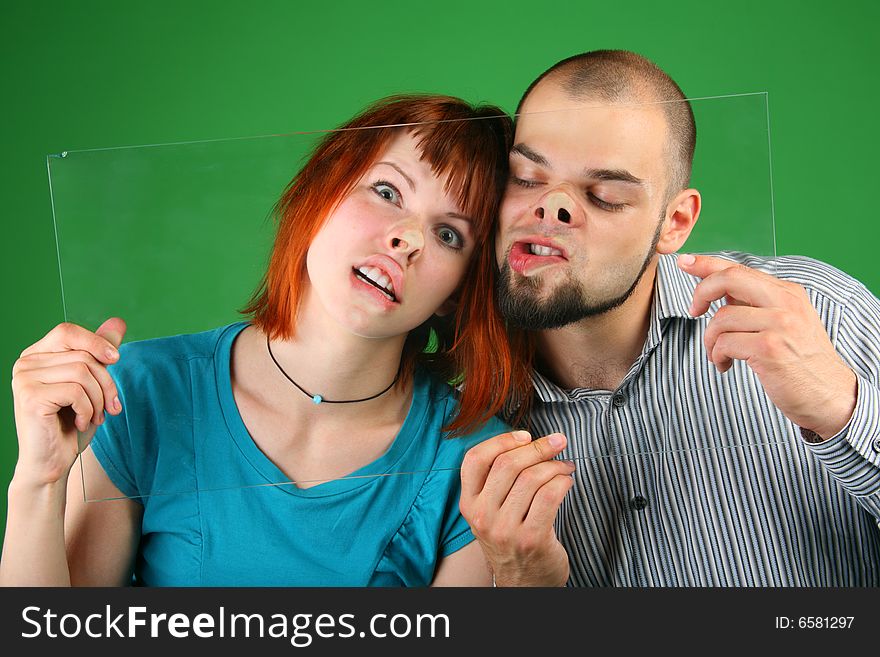 Close up girl with red hair and guy grimace behind glass on green