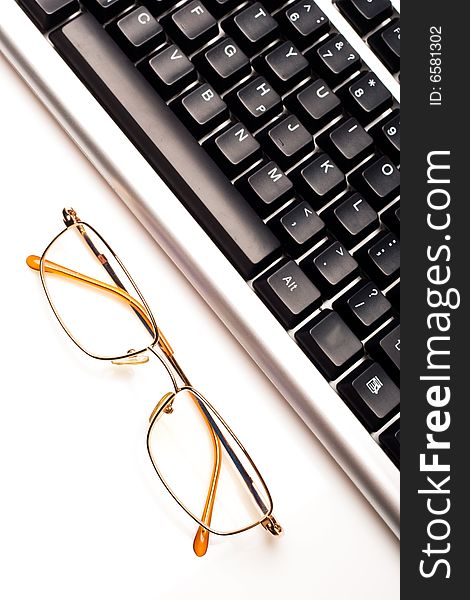 Fragment of keyboard with glasses, white background