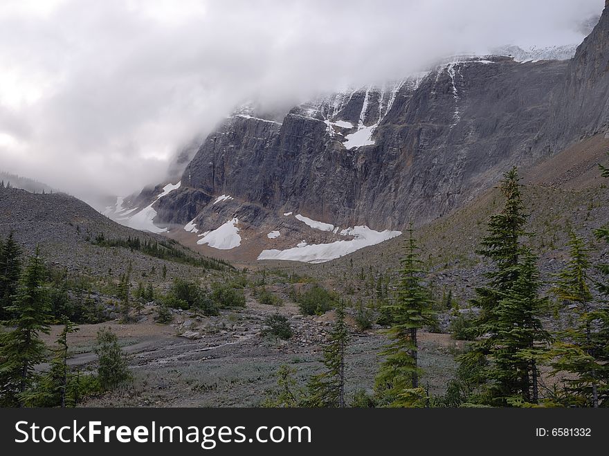 Mount Edith Cavell visible though the morning fog with alpine forest in the foreground. Jasper National Park, Canada. Mount Edith Cavell visible though the morning fog with alpine forest in the foreground. Jasper National Park, Canada