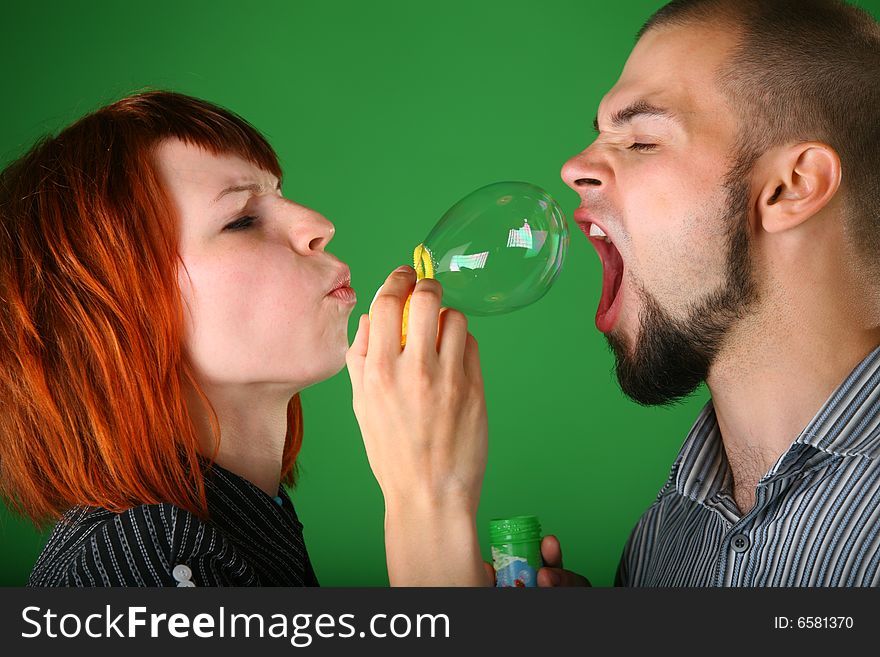 Girl with red hair blows soap bubble in mouth to guy on green. Girl with red hair blows soap bubble in mouth to guy on green