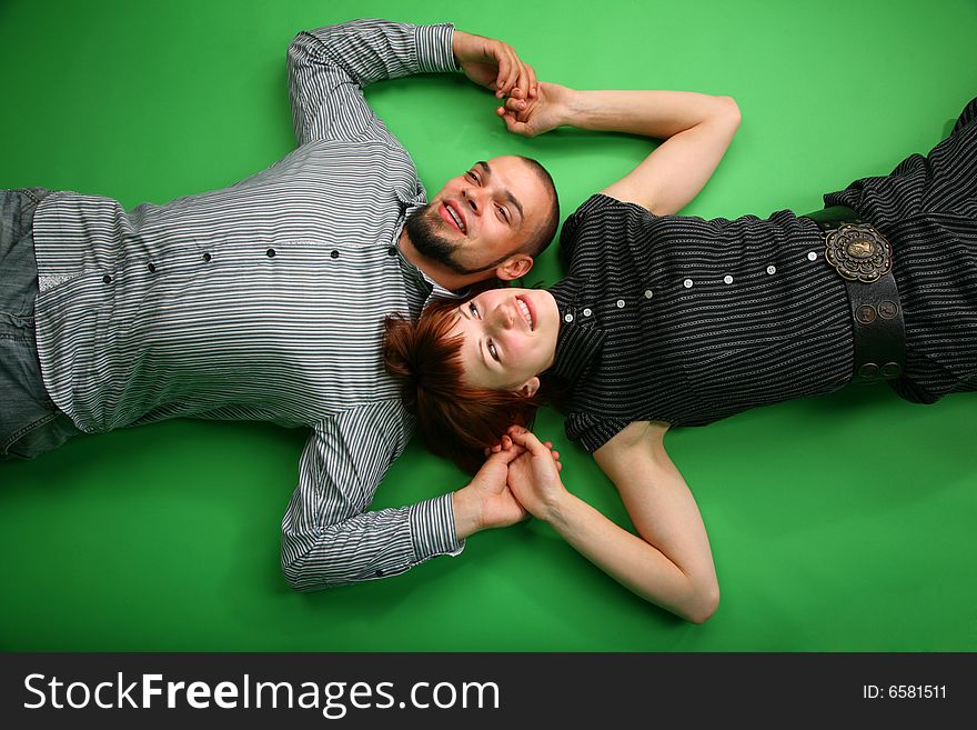 Girl with red hair and guy lie head to head and keep for hands on green. Girl with red hair and guy lie head to head and keep for hands on green