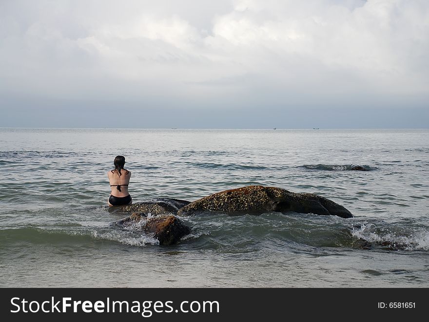 A woman sitting on a rock near the beach resort of Sihanoukville, Cambodia, watching the waves come in from the South China Sea.