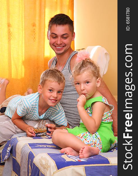 Two children with father sitting on bed in room