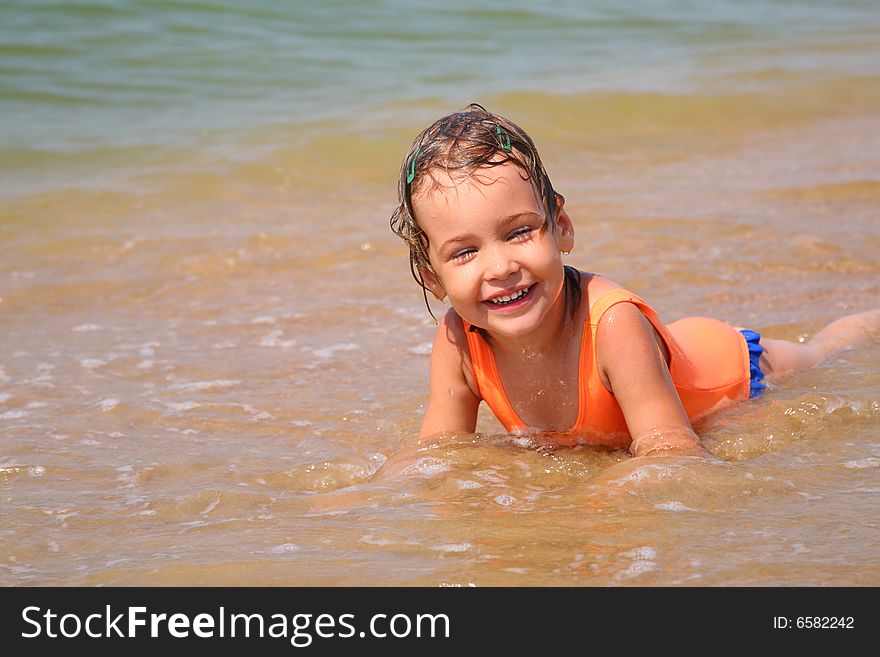 Little girl lies in waves on shore