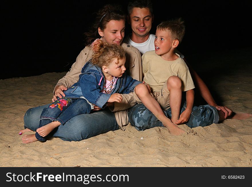 Parents with two children sit on sand at night