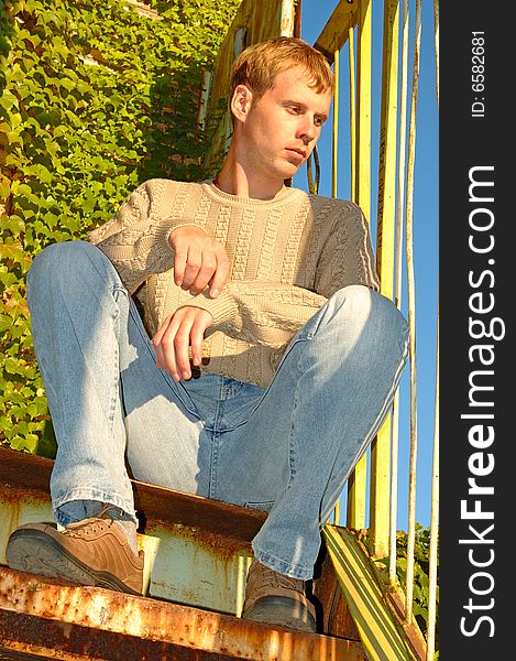 Young stylish blonde man sit on stairs near overgrown with vine wall. Young stylish blonde man sit on stairs near overgrown with vine wall.