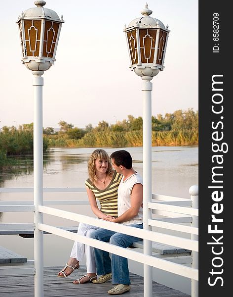 Pair on a pier. Look against each other and smile