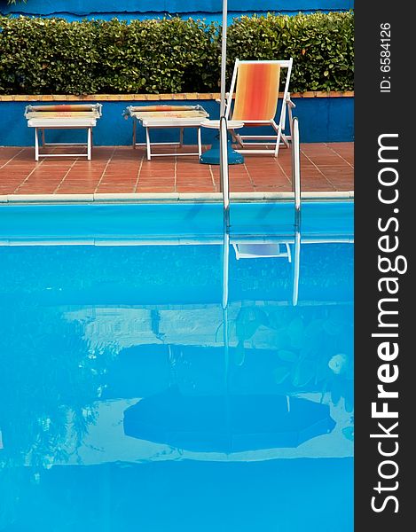 Hotel swimming pool with reflection and deck-chairs. Shallow depth of field