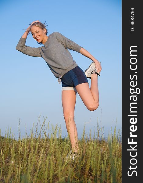 Athletics young woman stretching in a hilly meadow