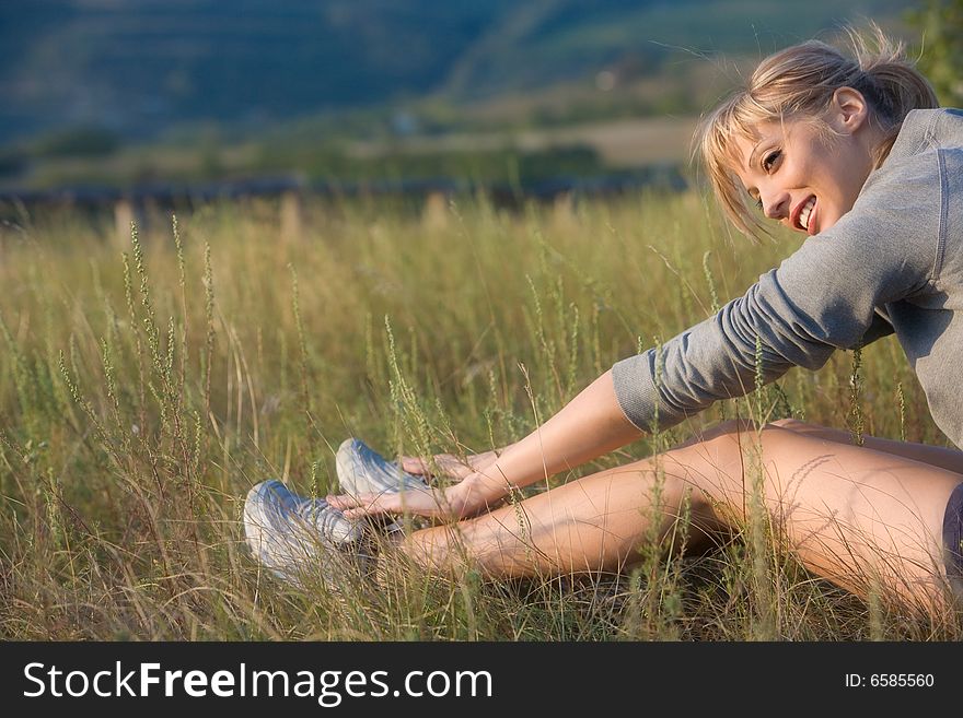 Sporty young woman stretching in a hilly meadow. Sporty young woman stretching in a hilly meadow