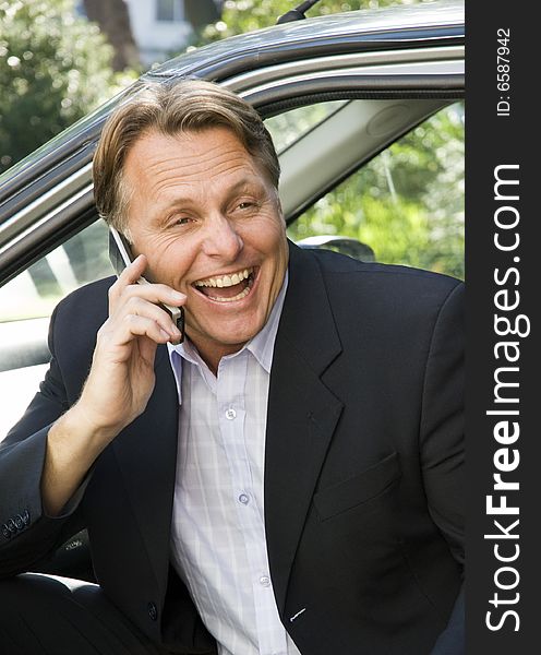 A businessman has a fun chat on his cellphone while he is sitting in his car. A businessman has a fun chat on his cellphone while he is sitting in his car