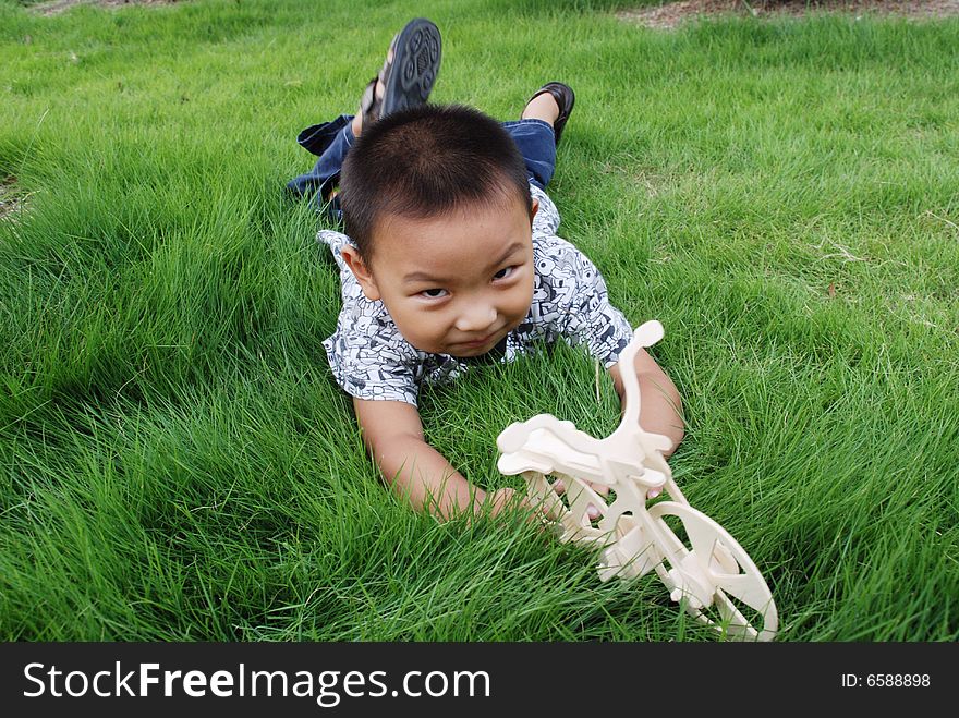 The boy grovels on the meadow playing with his toy happily. The boy grovels on the meadow playing with his toy happily.