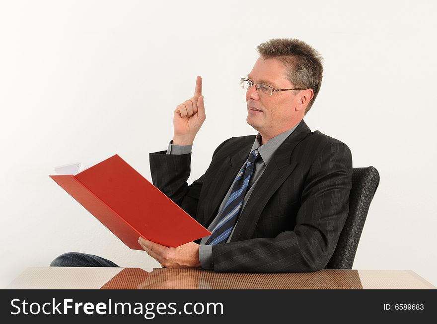 Business man at the office, reading company figures. Red book in his hand.