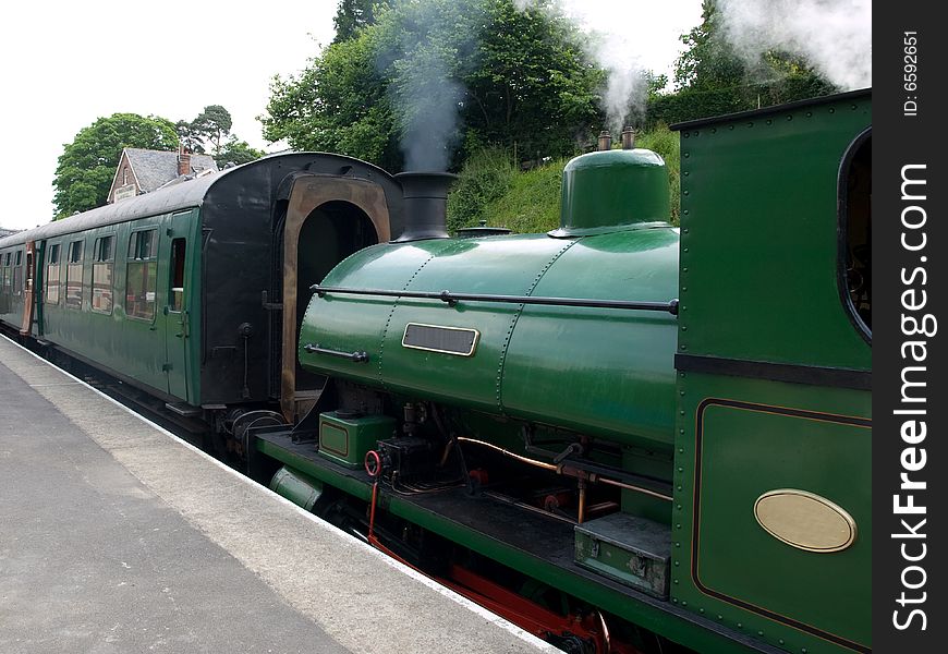 A green steam train and carriage at a station