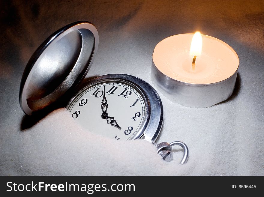 Antique watch covered with sand and a candle