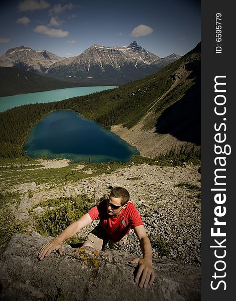 Young climber reaches for handhold on boulder, with turquoise alpine lakes in the background,  Canadian Rocky Mountains. Young climber reaches for handhold on boulder, with turquoise alpine lakes in the background,  Canadian Rocky Mountains