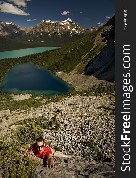 Young climber reaches for handhold on boulder, with turquoise alpine lakes in the background,  Canadian Rocky Mountains. Young climber reaches for handhold on boulder, with turquoise alpine lakes in the background,  Canadian Rocky Mountains