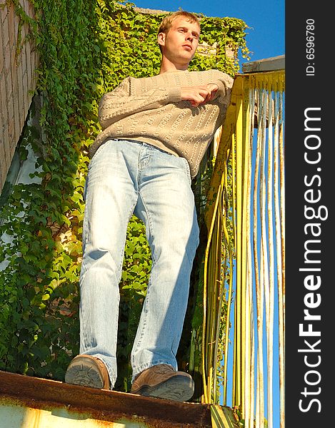 Young stylish blonde man stay on stairs near overgrown with vine wall. Young stylish blonde man stay on stairs near overgrown with vine wall.