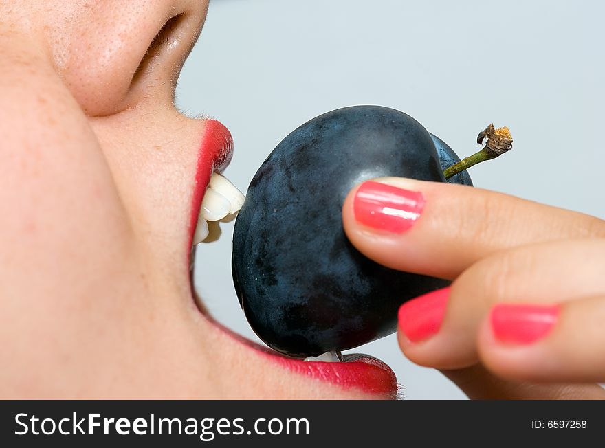 Girl, holding a plum between her teeth, taking a bite. Girl, holding a plum between her teeth, taking a bite