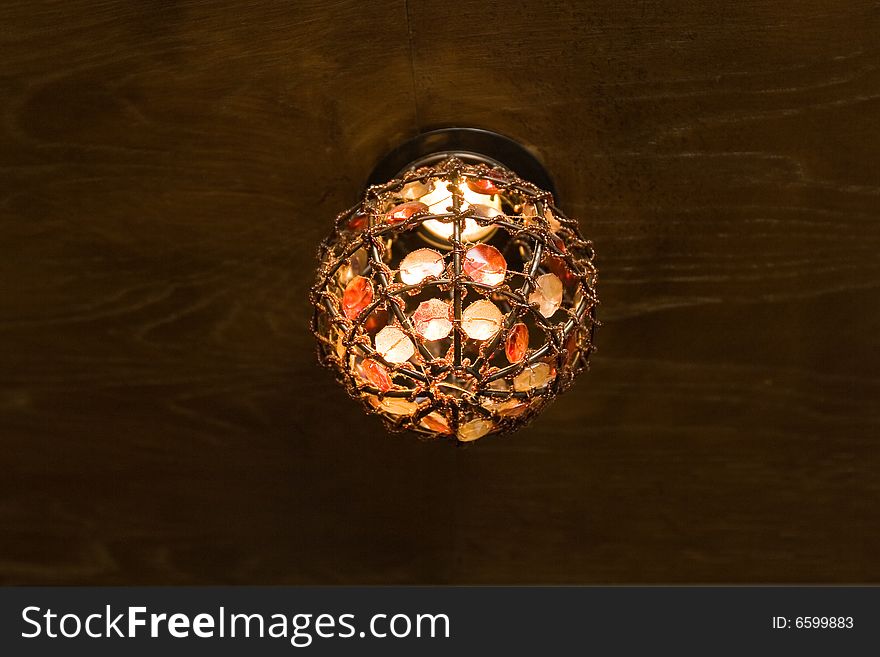 Lamp from a multi-coloured glass on a wooden ceiling