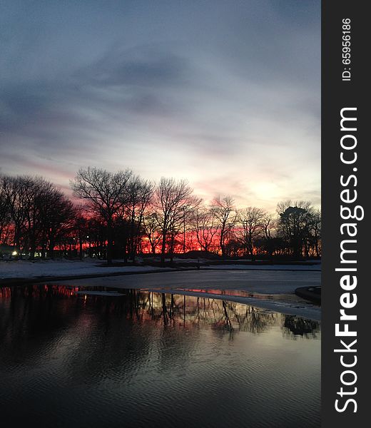 Sunset In A Park With Ice On Frozen Pond In Winter.