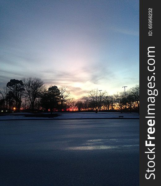 Sunset in a Park with Ice on Frozen Pond in Winter.