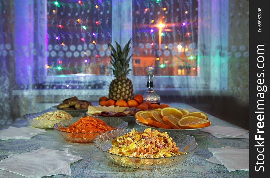 Festively laid table with salads, pineapple, meat, wine and tangerines at night. Festively laid table with salads, pineapple, meat, wine and tangerines at night