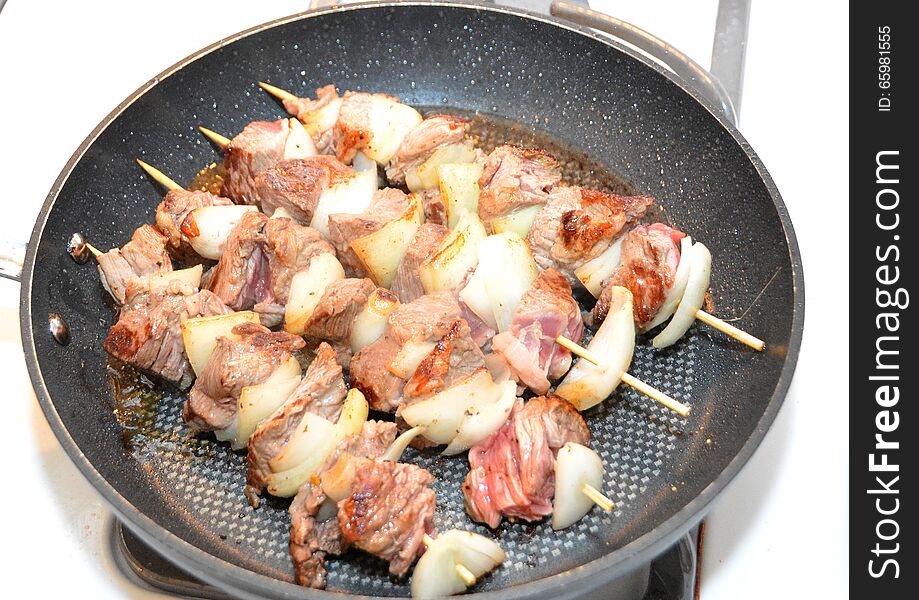 Four shashlik skewers roasting in a frying pan. Four shashlik skewers roasting in a frying pan