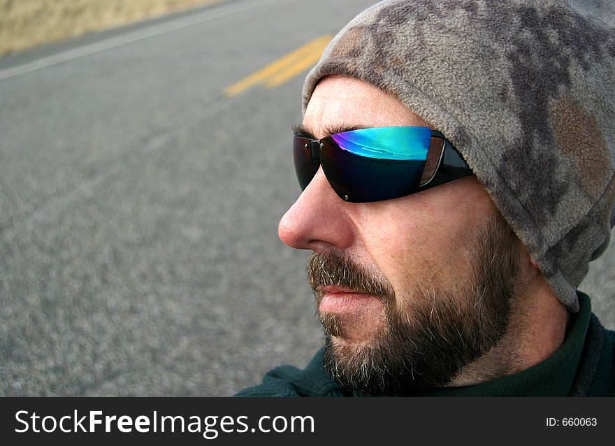 A middle-aged man with cool shades and a beanie looks forward to a road trip. Pavement and highway markings in the background. The sky and road ahead suggested in the reflection. For those who love to drive!. A middle-aged man with cool shades and a beanie looks forward to a road trip. Pavement and highway markings in the background. The sky and road ahead suggested in the reflection. For those who love to drive!