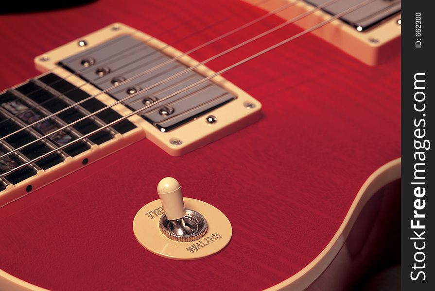 The detail of a red electric guitar showing strings, pickup and rhythm/treble switch. The detail of a red electric guitar showing strings, pickup and rhythm/treble switch