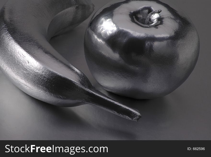 A metallic-looking banana and apple on a silver surface.