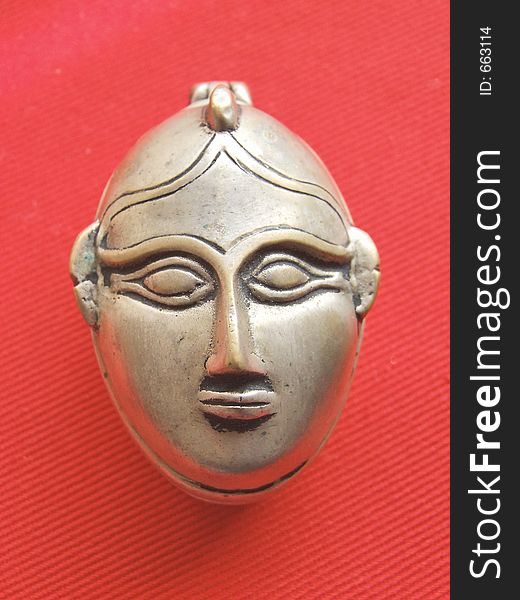 A small silver box with a carved face against a red cloth