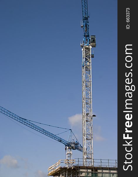 Two tall cranes tower over a construction site with blue sky in background. Two tall cranes tower over a construction site with blue sky in background