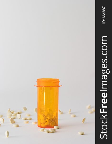 Medicine bottle on table with tablets around it; bottle is placed in the center of the frame with some pills in the bottle and some laying around it. Medicine bottle on table with tablets around it; bottle is placed in the center of the frame with some pills in the bottle and some laying around it