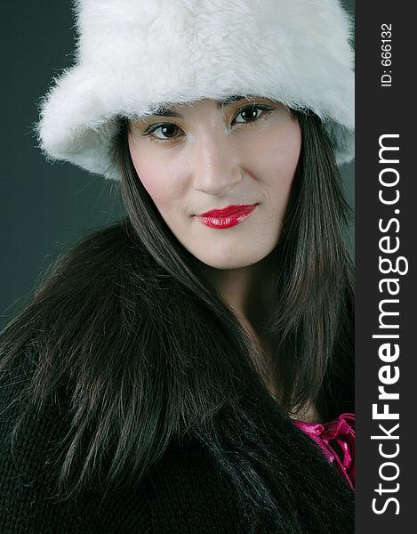 Beautiful brunette with asian features poses confidently with a white fur hat and an expression of arrogance. Beautiful brunette with asian features poses confidently with a white fur hat and an expression of arrogance