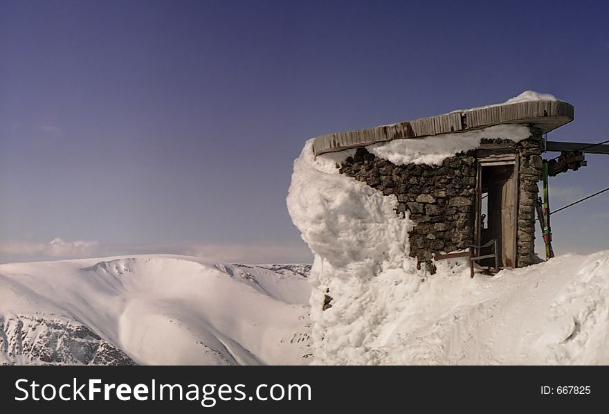 Stone construction in mountains at the end of precipice. Structure from a stone in a snow valley. Shelter at top of a mountain. Stone construction in mountains at the end of precipice. Structure from a stone in a snow valley. Shelter at top of a mountain.