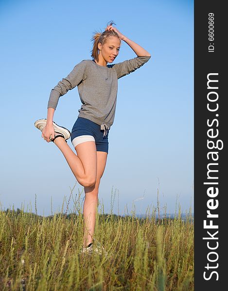 Athletics young woman stretching in a hilly meadow.