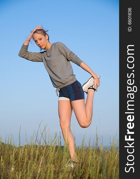 Athletics young woman stretching in a hilly meadow