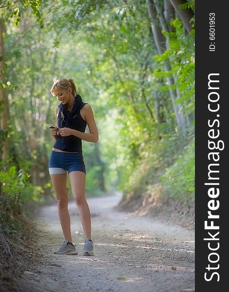 Sporty young woman listening music on mp3 player among a woods trail