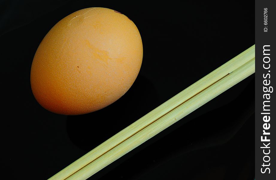 Irony asian diet concept - raw and little bit - egg on black plate and chopsticks. Irony asian diet concept - raw and little bit - egg on black plate and chopsticks