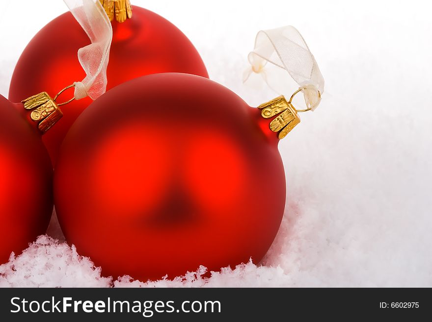 Red Christmas baubles on snow with gold ribbon hangers