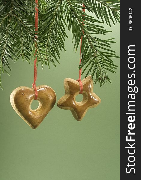 Two gingerbread cookies hanging under fir branch and isolated against green paper. Two gingerbread cookies hanging under fir branch and isolated against green paper