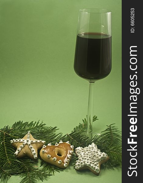 A glass of red wine and three decorated cookies with fir branch isolated on green paper. A glass of red wine and three decorated cookies with fir branch isolated on green paper