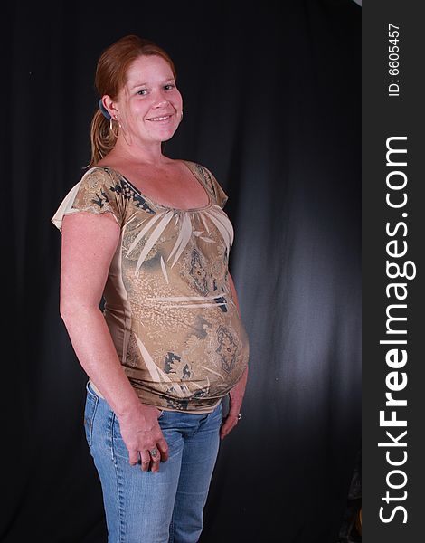 Young women with her hands in her jeans on a black background with a baby in her tummy. Young women with her hands in her jeans on a black background with a baby in her tummy