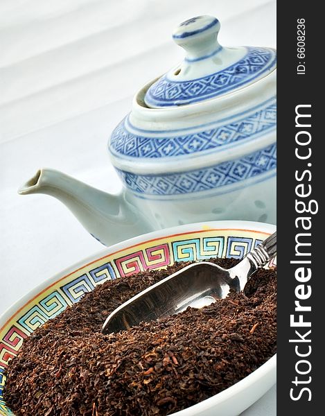 Tea leaves in bowl with teapot in the background. White backdrop and shallow depth of field. Tea leaves in bowl with teapot in the background. White backdrop and shallow depth of field